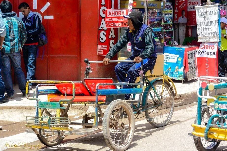 Peruvian Tricycle Taxi Driver in Vibrant Market Street — Fine art canvas print by Naomi McLeod